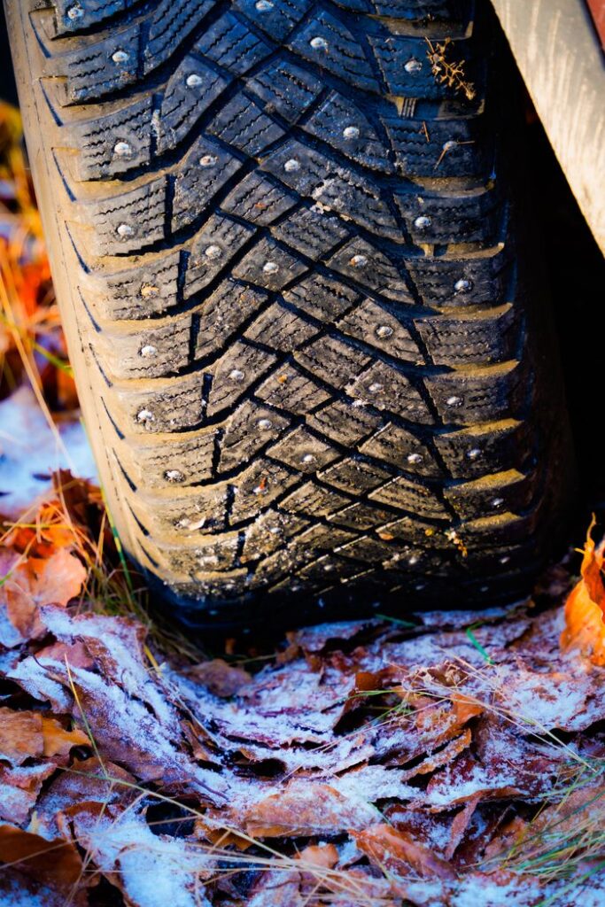 Close-up of a car tire on frosty autumn leaves, showcasing winter readiness.